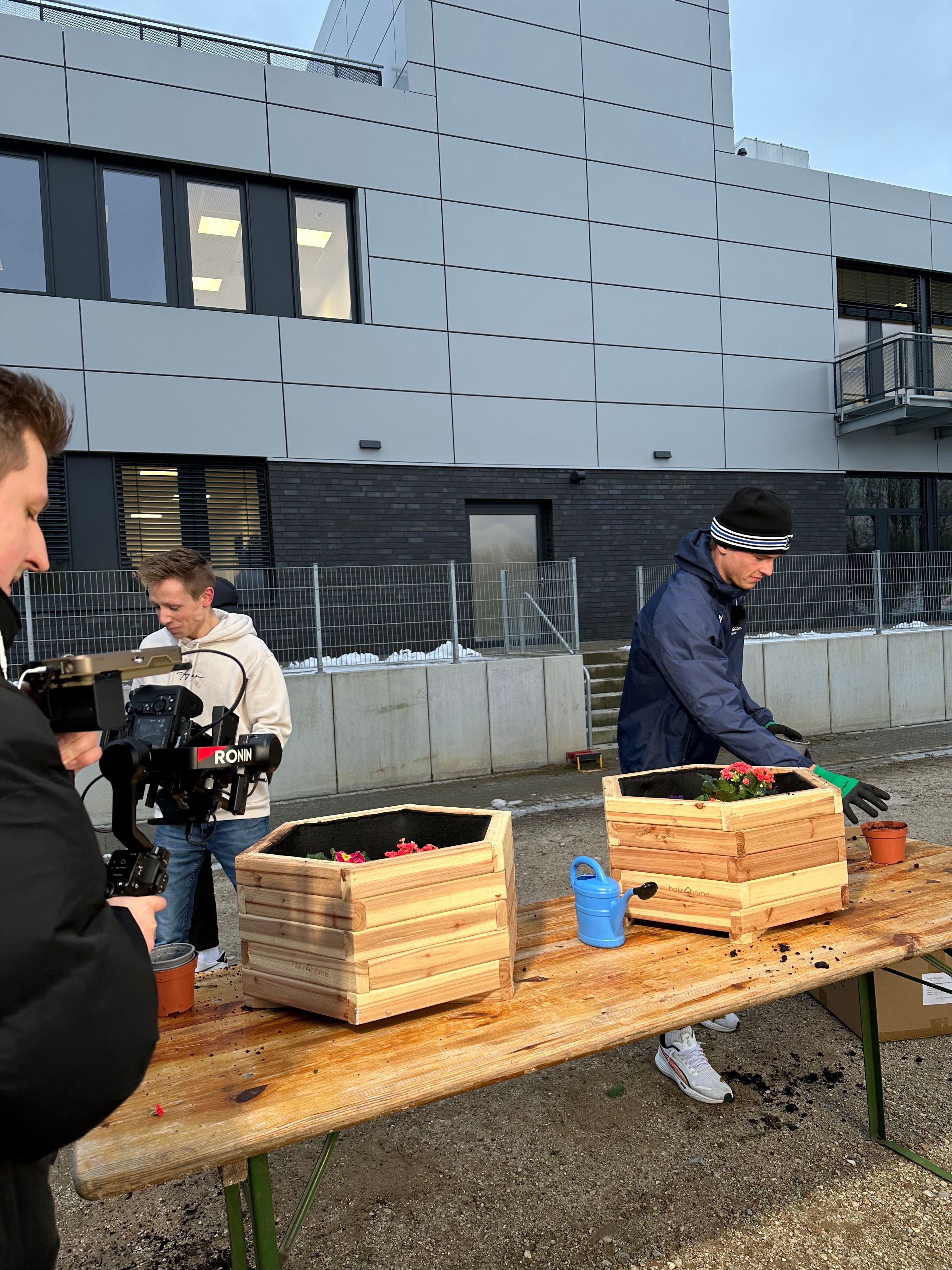 Team filmt das Bepflanzen von Holz-Pflanzkästen auf einer Bierzeltgarnitur vor dem Firmengebäude