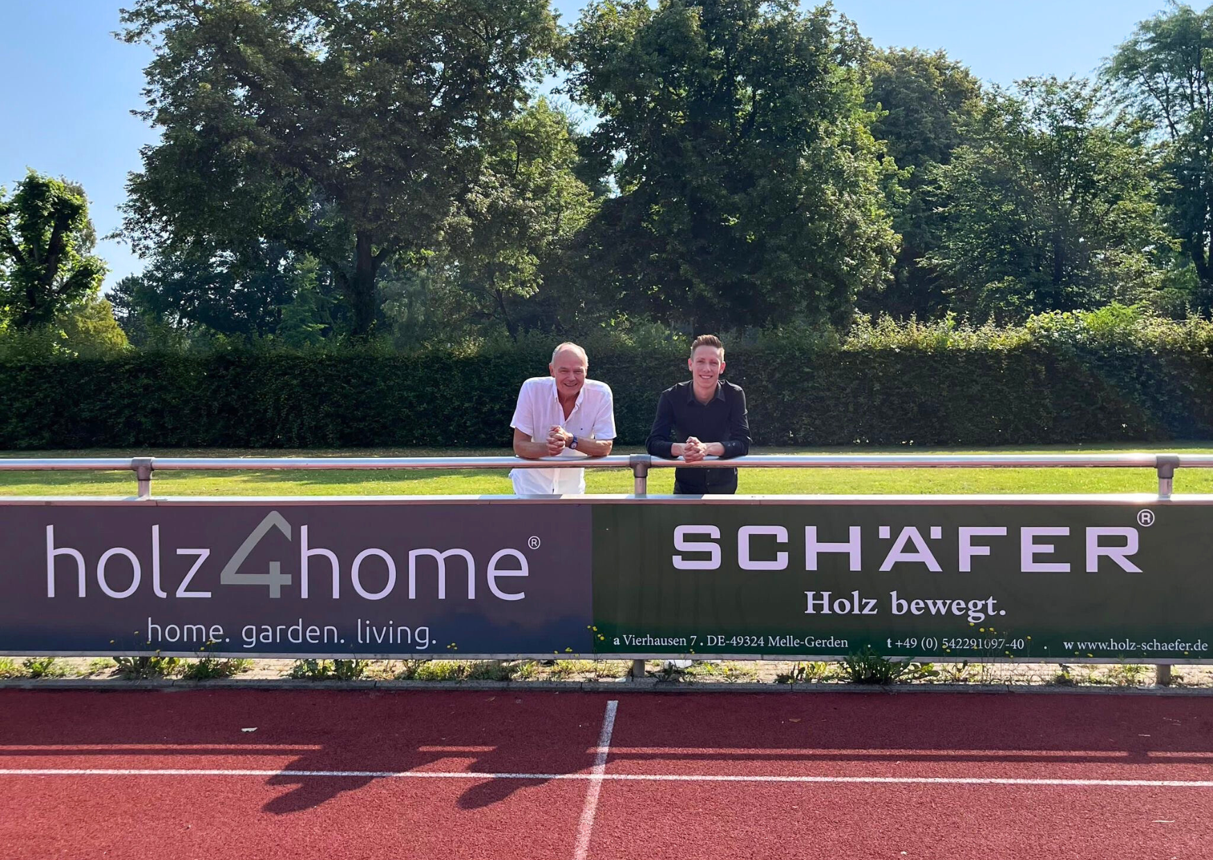 Zwei Männer hinter einer holz4home- und Schäfer-Werbebande am Sportplatz des SC Melle 03