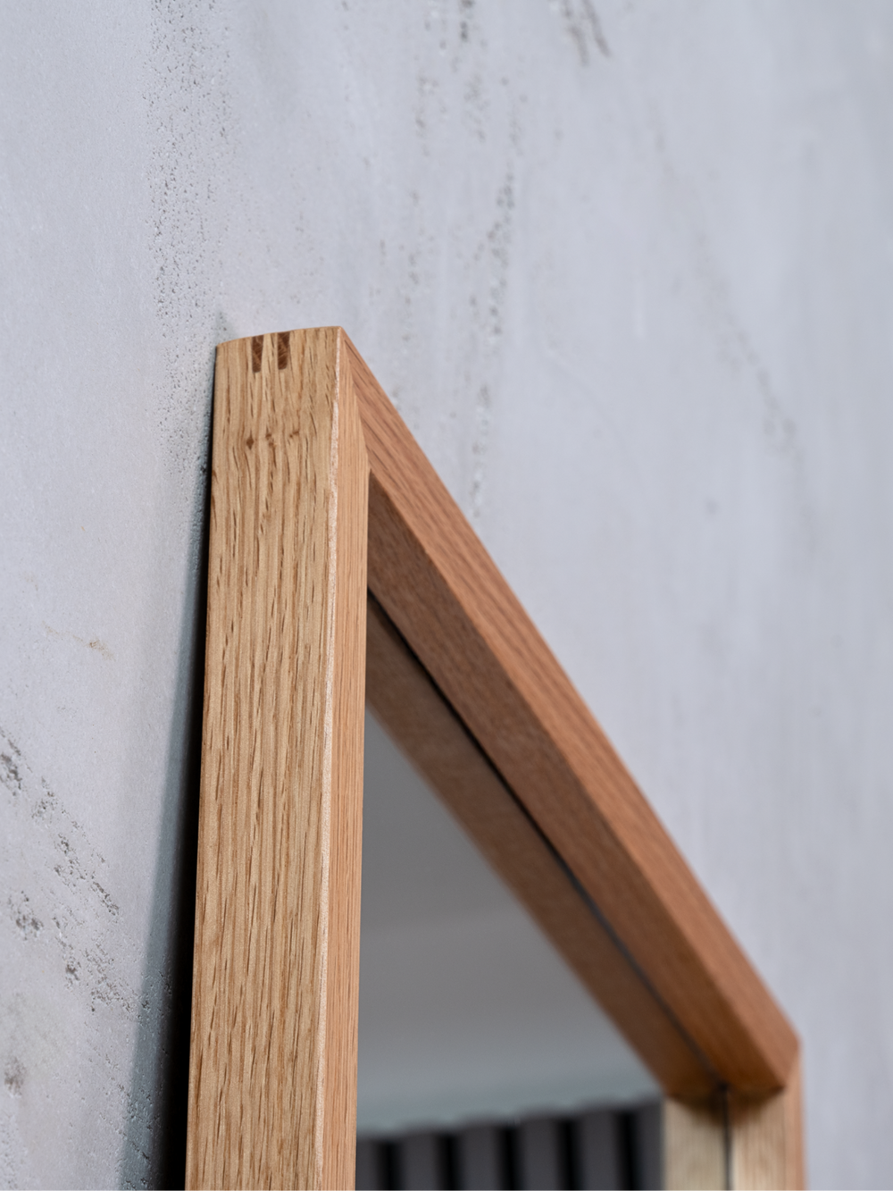 Detailaufnahme der oberen Ecke des Eichenrahmens am Wandspiegel vor einer grauen Betonwand